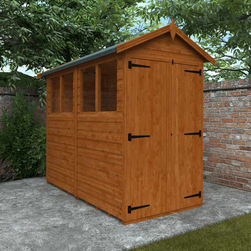Wooden shed with a gabled roof in a garden setting with trees and a brick wall.