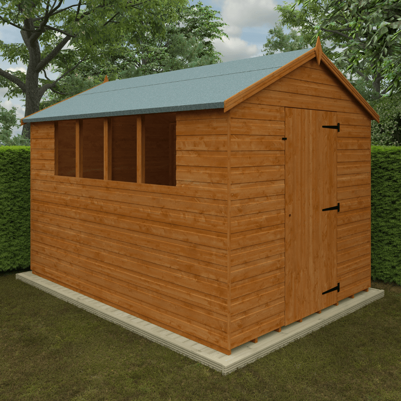 Wooden shed with a green roof on a grassy area with trees in the background