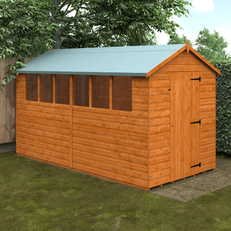 Wooden shed with a green roof on a grassy area with trees in the background