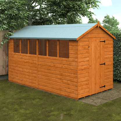 Wooden shed with a green roof on a grassy area with trees in the background